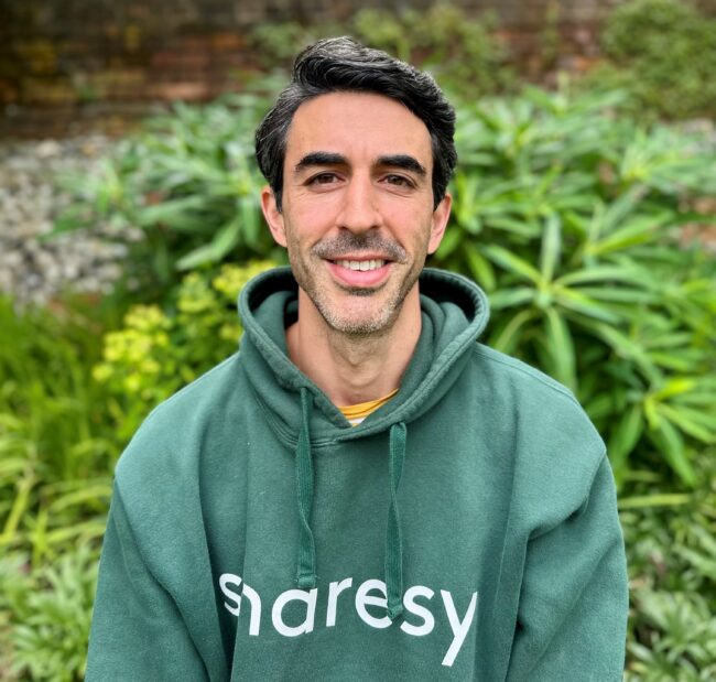 man in green sweatshirt sitting in garden in front of plants